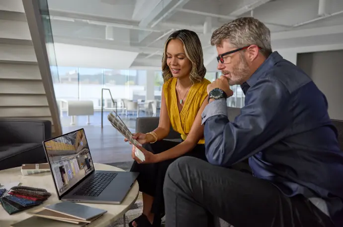 Réunion de travail professionnelle entre collègues dans bureau moderne avec vue panoramique. Femme en chemisier jaune et homme à lunettes analysent documents et données sur ordinateur portable dans environnement corporatif contemporain.
