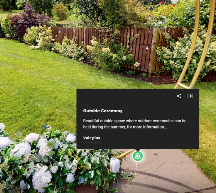 Jardin extérieur verdoyant et soigné, idéal pour des cérémonies en plein air estivales. L&#39;image présente une pelouse bien entretenue, bordée de massifs fleuris (roses blanches, arbustes variés) et d&#39;une haie végétale dense en arrière-plan. Une clôture en bois naturel délimite l&#39;espace, ajoutant une touche rustique et intimiste. Au premier plan, une allée en dalles de pierre guide les invités vers l&#39;espace de cérémonie. Parfait pour illustrer les mots-clés : mariage en extérieur, lieu de réception jardin, décoration cérémonie estivale, espace vert événementiel, location cérémonie nature, ambiance romantique et champêtre.