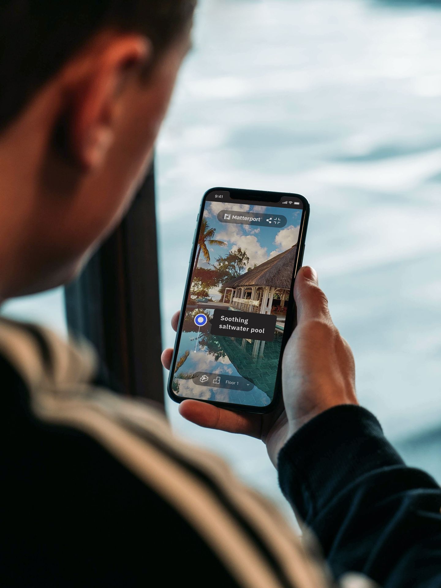 Découverte immersive d’un hôtel de luxe via une application mobile de réalité augmentée (AR) : vue en temps réel d’un smartphone affichant une superposition AR d’une piscine à débordement et d’un bungalow tropical avec toit de chaume. L’écran montre une navigation intuitive (flèche bleue, menu Matterport) et des annotations interactives comme ‘Soothing saltwater pool’. Idéal pour illustrer les innovations technologiques dans le tourisme, l’expérience client digitale ou les solutions AR pour l’hôtellerie. Mots-clés associés : réalité augmentée voyage, visite virtuelle hôtel, application mobile tourisme, expérience immersive client, Matterport AR, piscine hôtel luxueux, bungalow tropical.